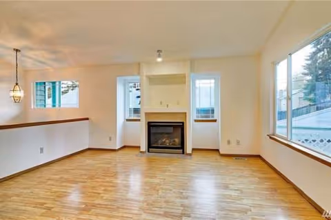 Bright open living room with hardwood floors, a fireplace, large windows, and pendant lights.