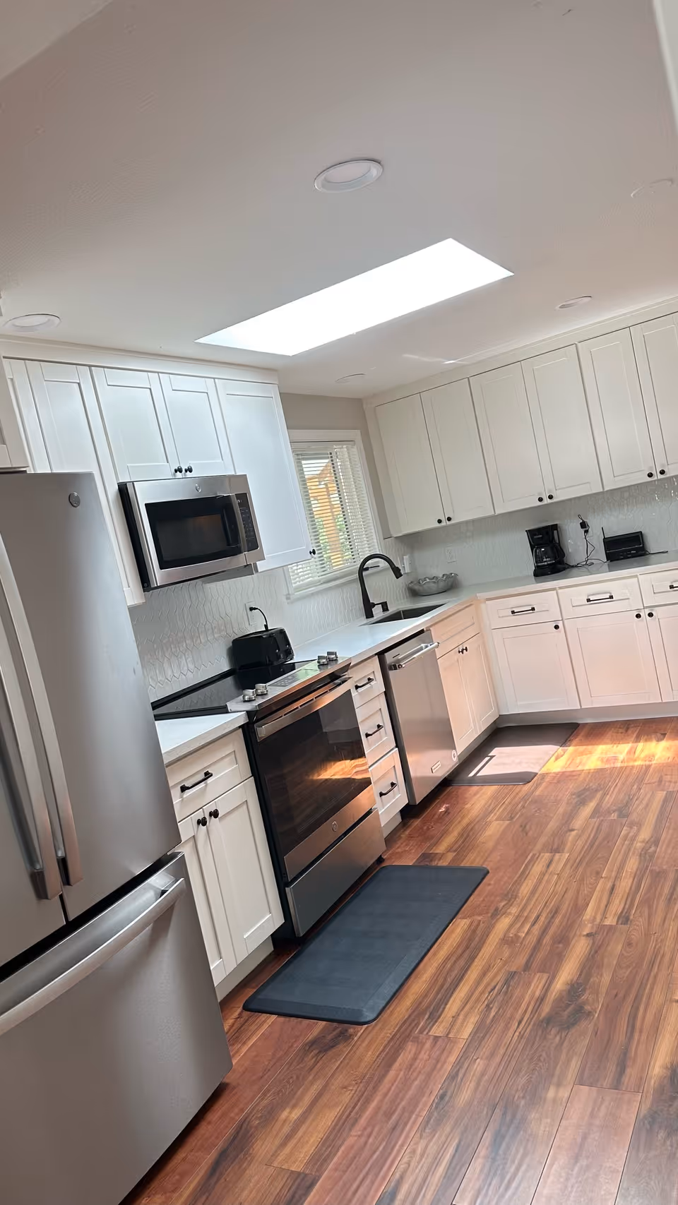 Bright modern kitchen with white cabinets, stainless steel appliances, a skylight, and wood-look flooring.