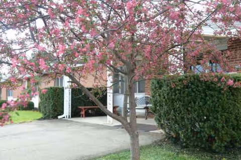 Front view of a brick senior living building with a pink flowering tree and benches.