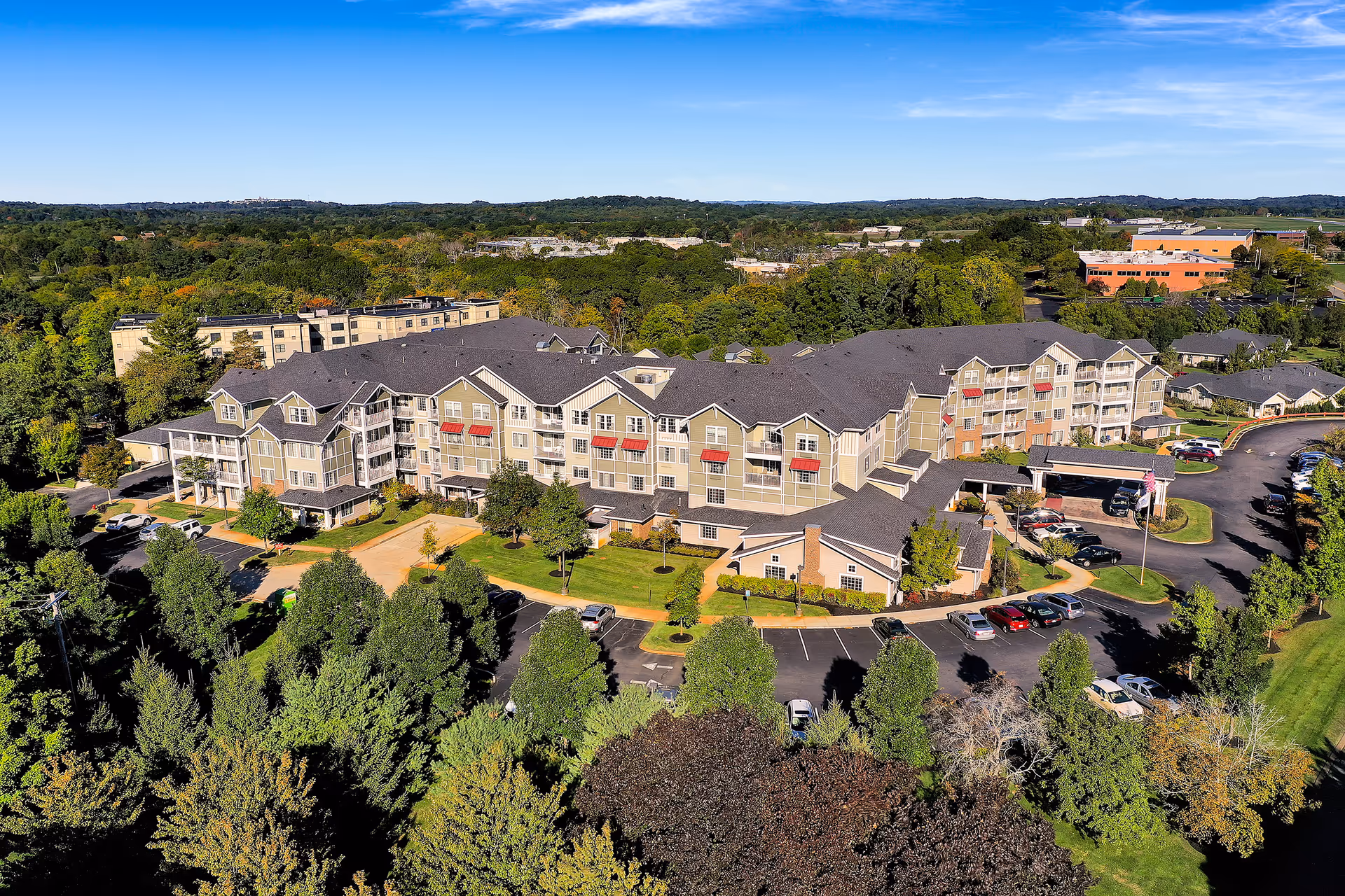 Aerial view of Colonial Gardens Gracious Retirement Living complex with beige buildings, parking, and trees.