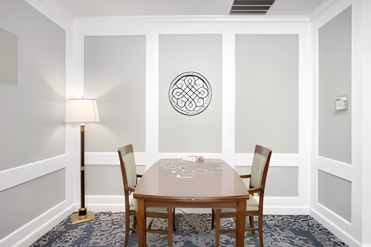 Small dining/meeting room with a wooden table, two chairs, a floor lamp, and decorative wall paneling.