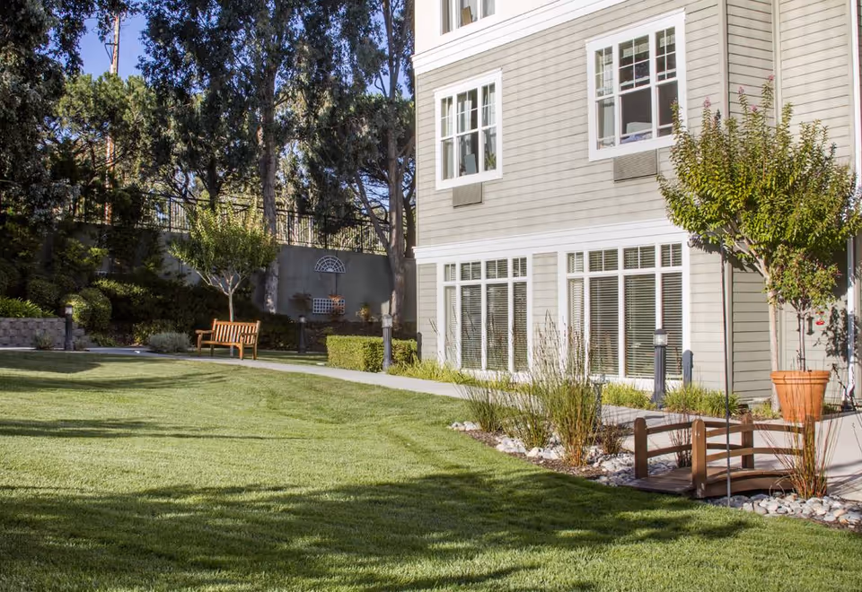 Well-maintained lawn and landscaped courtyard beside a multi-story senior living building with benches and large windows.