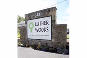 Stone monument sign for Luther Woods Nursing & Rehabilitation Center with the address number 313 displayed on top, surrounded by small flowers and greenery.