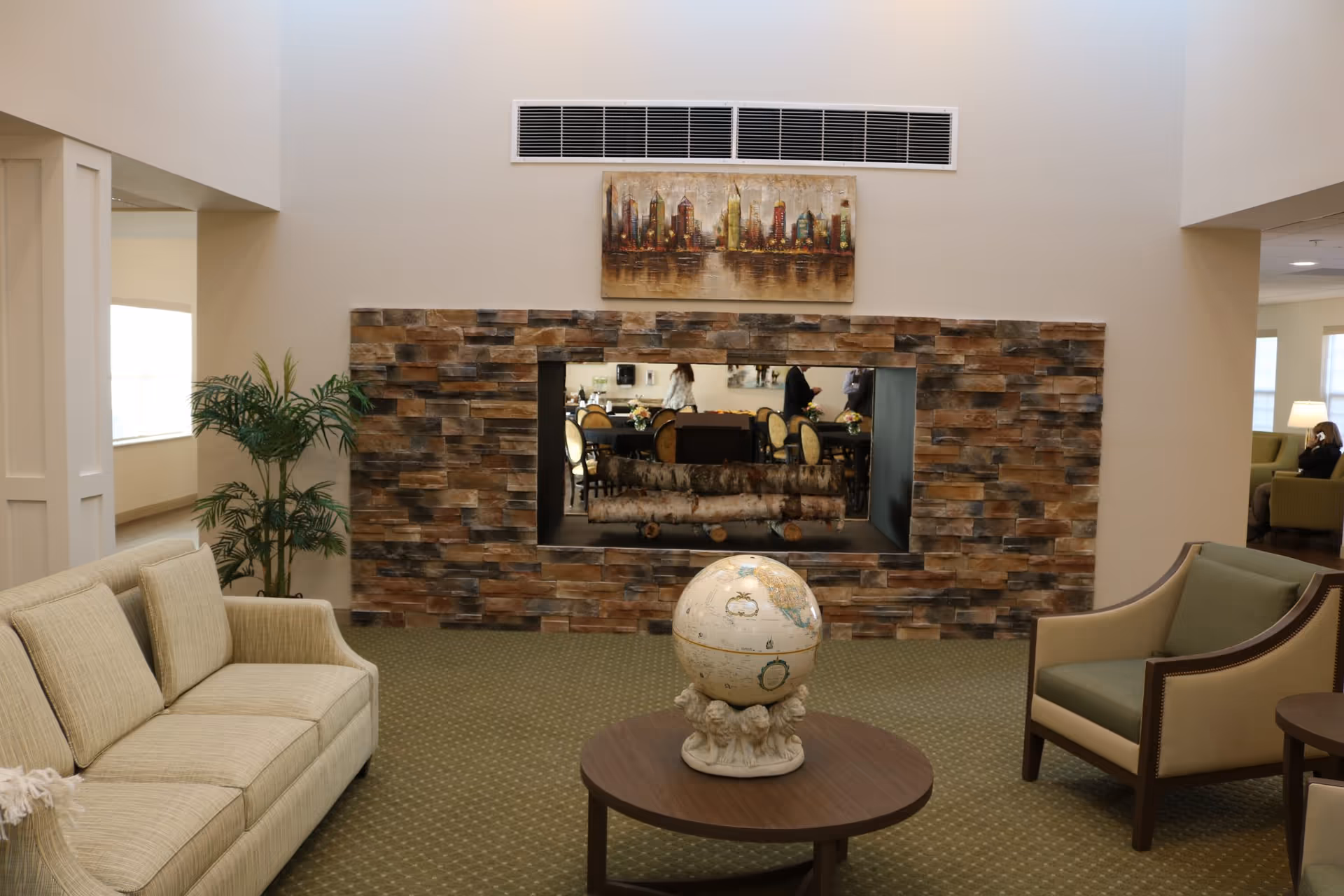 Seating area with sofas and armchairs around a coffee table holding a decorative globe, facing a stone-clad fireplace opening in a communal living room.