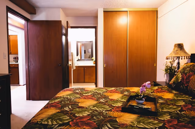 A brightly decorated bedroom with floral bedding, showcasing a view towards the bathroom and a closet.