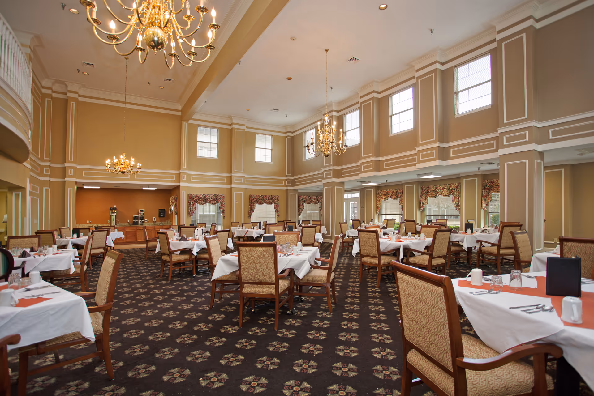 Spacious formal dining room with multiple tables set with white tablecloths, chandeliers, and tall windows.