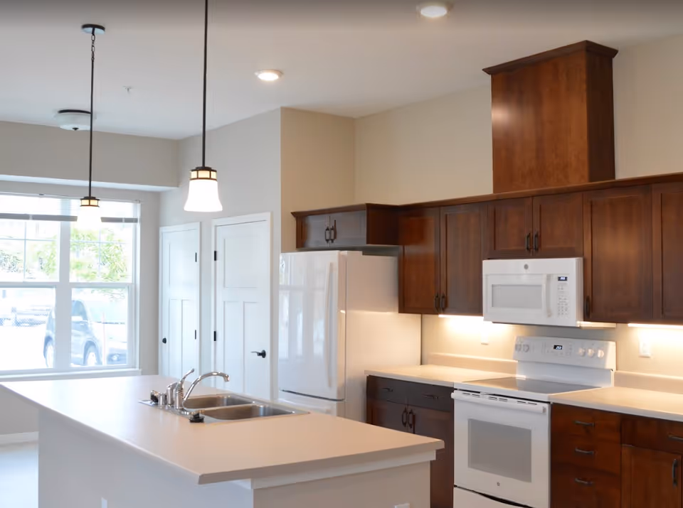 Bright modern kitchen with dark wood cabinets, white appliances, a large island with sink, and pendant lights over the counter.