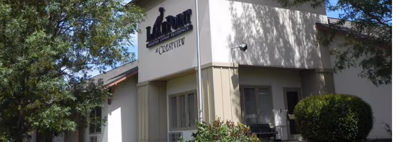 Exterior view of the Homestead Assisted Living & Memory Care of Crestview building with trees and bushes in the foreground under a clear sky.