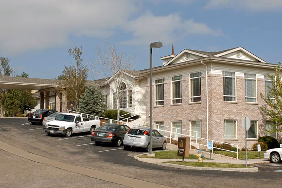 Exterior front of a brick senior living facility showing the entrance, wheelchair ramp, and parked cars.