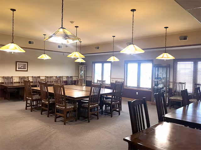 Spacious communal dining room with wooden tables and chairs illuminated by multiple hanging pendant lights.