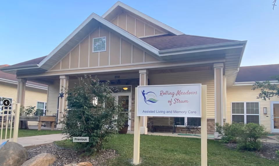 Front view of Rolling Meadows of Strum assisted living facility with sign and benches.
