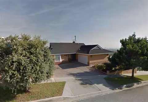 Front exterior of Carezza Guest Home with driveway, trees, and a clear sky.