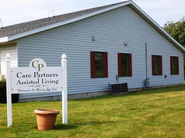White single-story building with red-trim windows and a lawn sign reading "Care Partners Assisted Living".