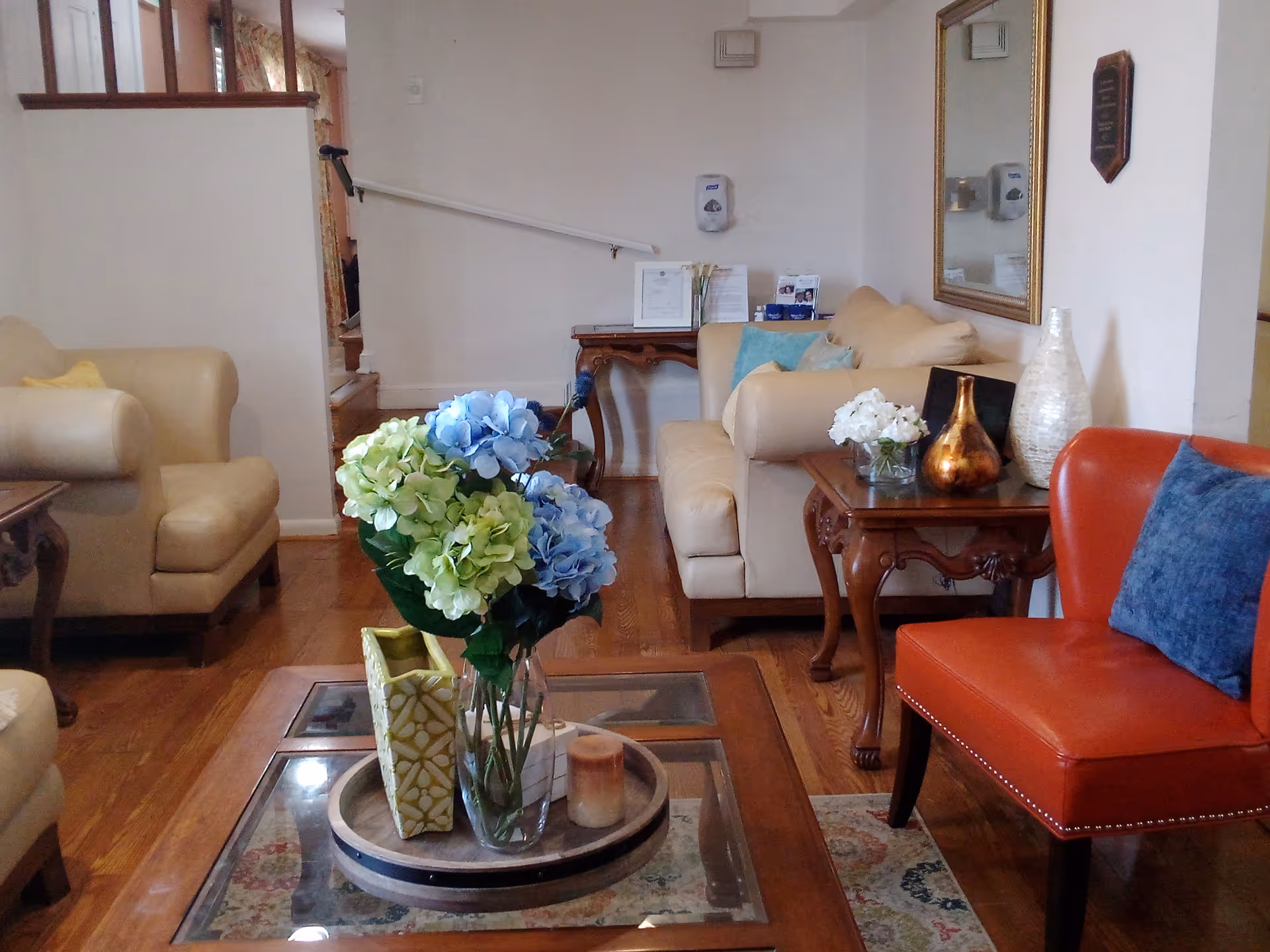 Cozy lounge area with beige sofas, red chair, glass coffee table, and hydrangea décor.