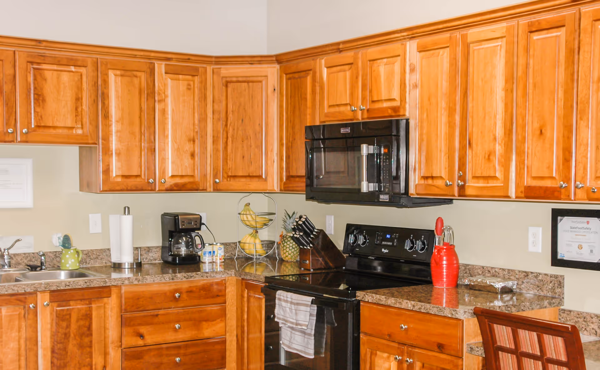 Kitchen with wooden cabinets, black stove and microwave, sink, coffee maker, and countertop accessories.