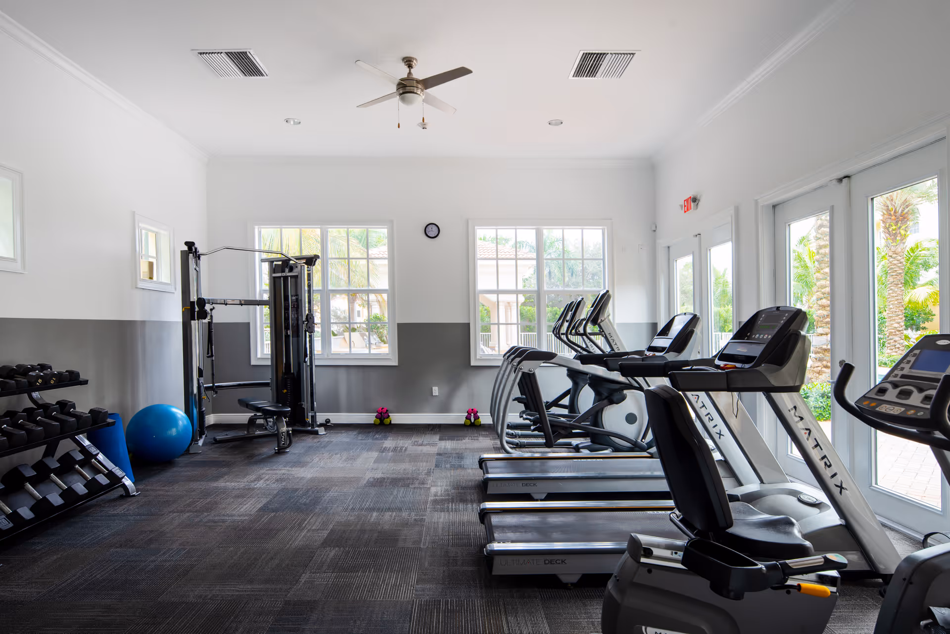 Bright fitness room with treadmills, weight rack, exercise machines and windows looking outside.