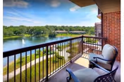 Balcony with two cushioned chairs and a small table overlooking a lake, fountain, and landscaped grounds.