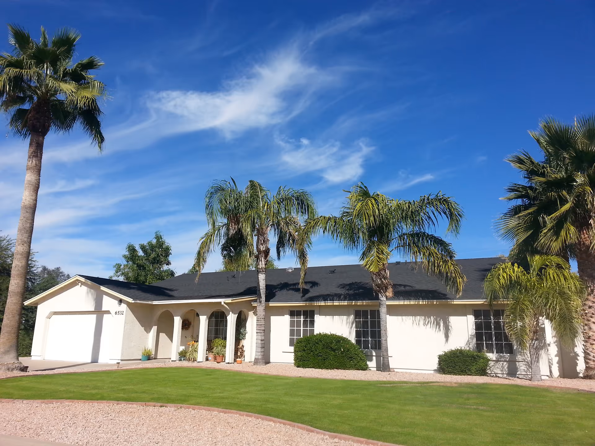 Single-story white house with palm trees, a green lawn, and a bright blue sky.