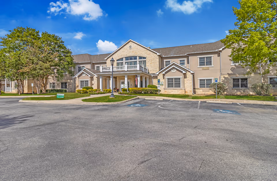 Front exterior of a two-story senior living facility with a driveway, landscaped entrance, and blue sky.