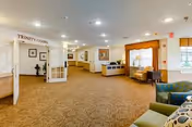 Well-lit senior living facility common area with seating, a reception desk, and a hallway.