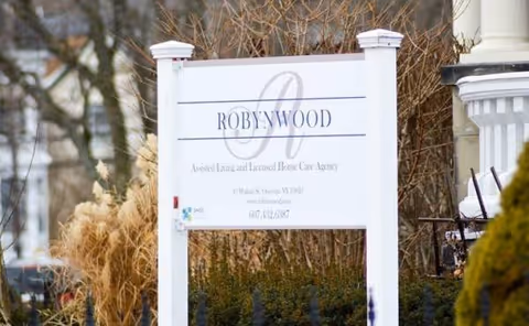 Robynwood Assisted Living Community sign on a front lawn with bare shrubs.