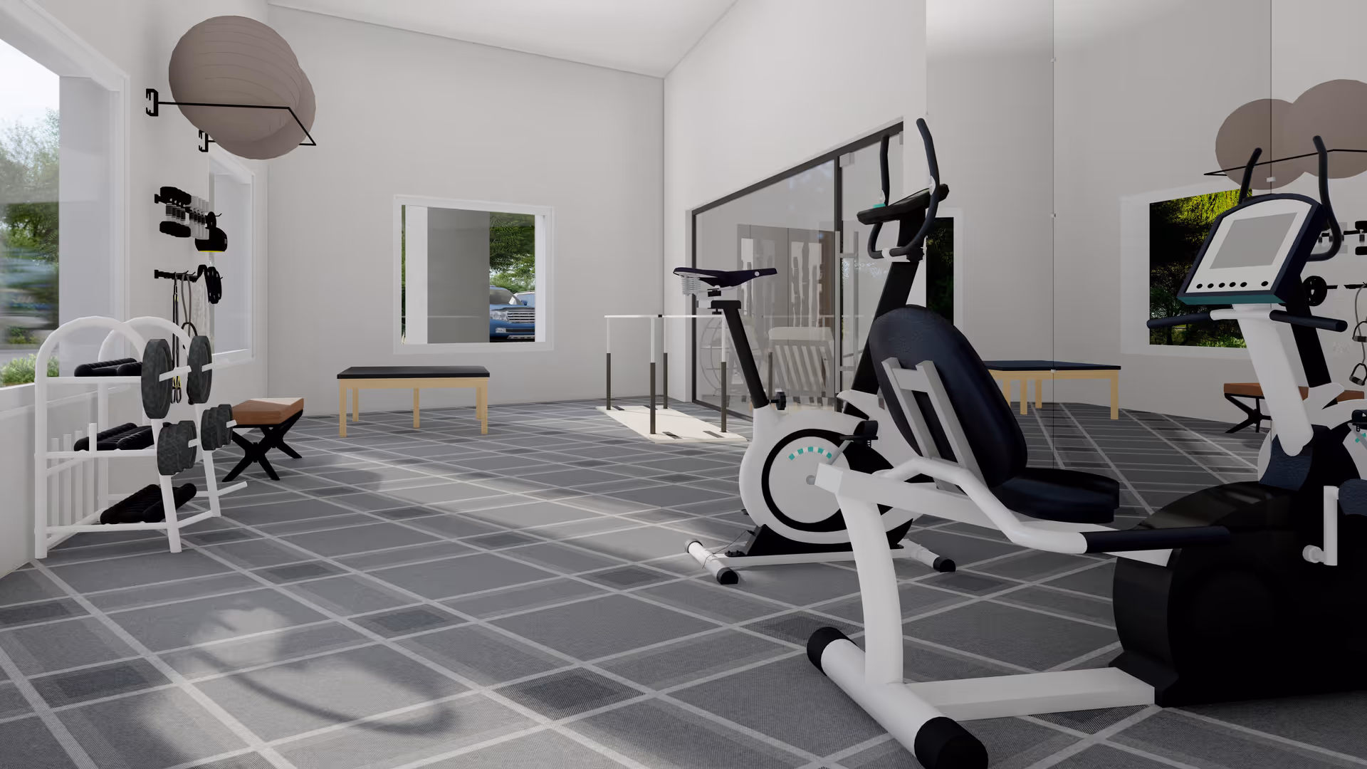 A bright exercise room with large windows, featuring stationary exercise bikes, a bench, weights on a rack, and a large mirror on one wall. The floor has a gray checkered pattern, and the room has white walls with natural light coming in.