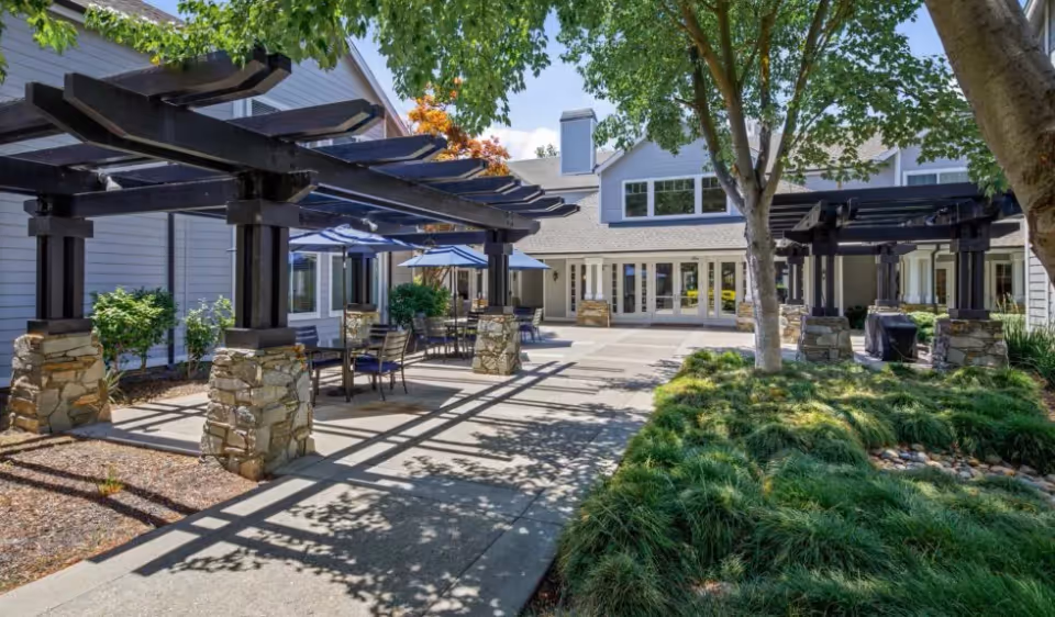 Outdoor courtyard at Oakmont Of Brookside with pergolas, patio tables and umbrellas in front of the building.