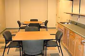 Small communal dining area with two tables, six chairs, and a kitchenette with sink and cabinets along one wall.