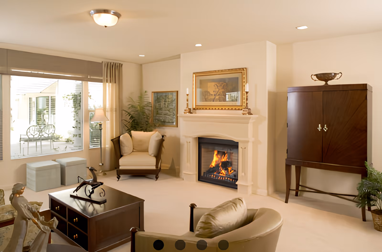 Sunlit living room with a lit fireplace, upholstered chairs, coffee table, and a large window overlooking a patio.