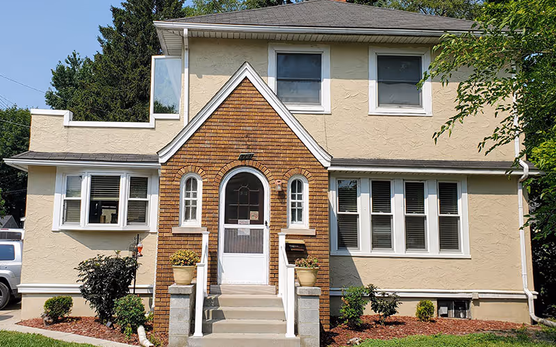 Beige two-story building with a brick central entry, arched doorway, and steps.
