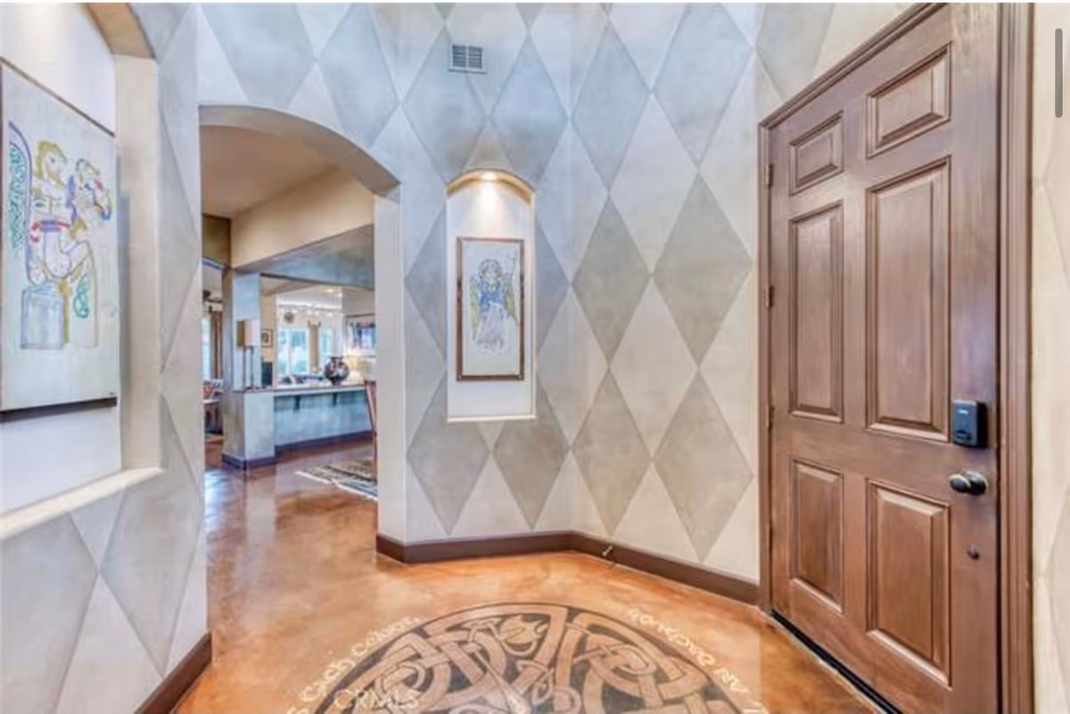 A welcoming entrance hall featuring decorative walls, artwork, and a wooden door.