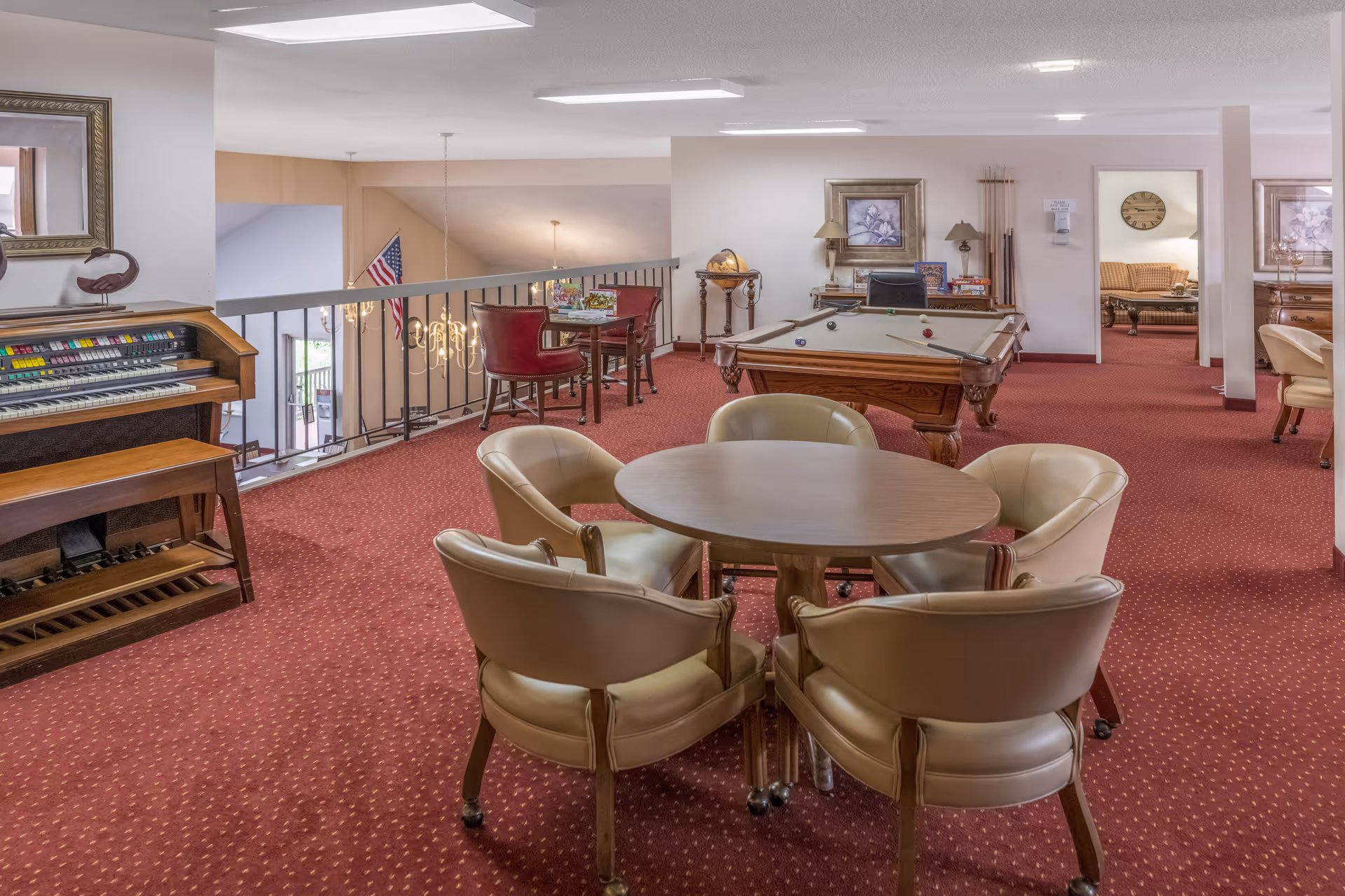 An upstairs common lounge with a round table and chairs, a pool table, an organ, and additional seating areas.