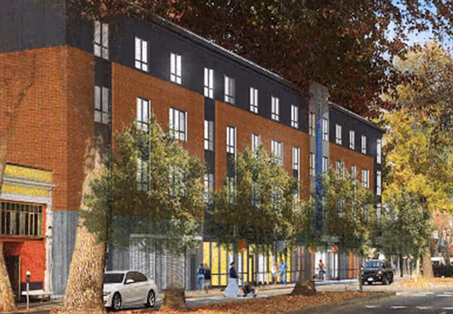 Exterior street view of a multi-story brick and dark-clad building with ground-floor glass storefronts, trees, parked cars, and pedestrians.