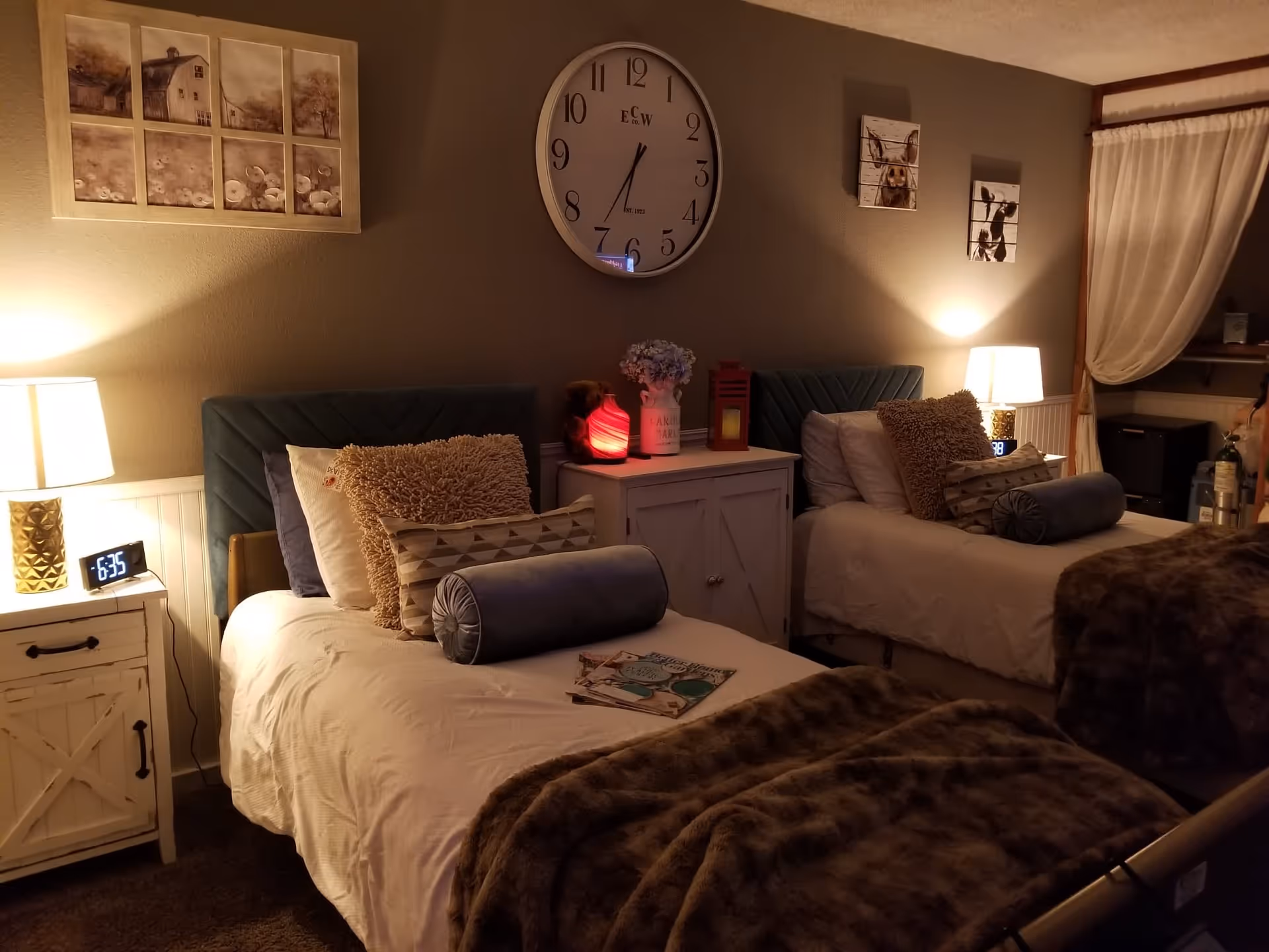 Cozy bedroom with two twin beds, bedside tables and lamps, decorative pillows and a large wall clock.