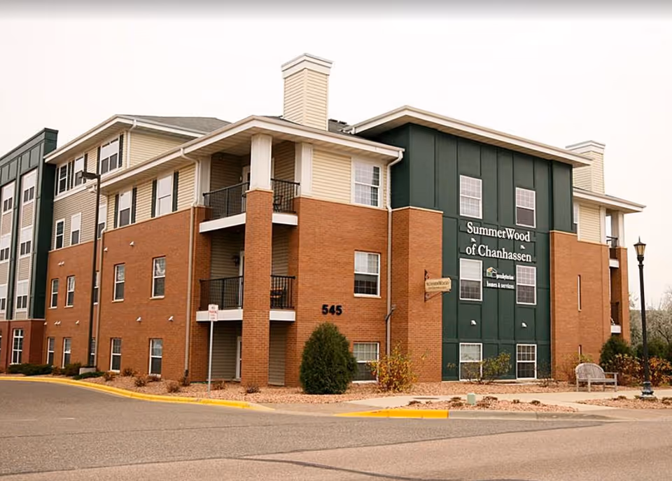 Front exterior of the SummerWood of Chanhassen senior living building with brick and green siding, balconies, and an entrance.