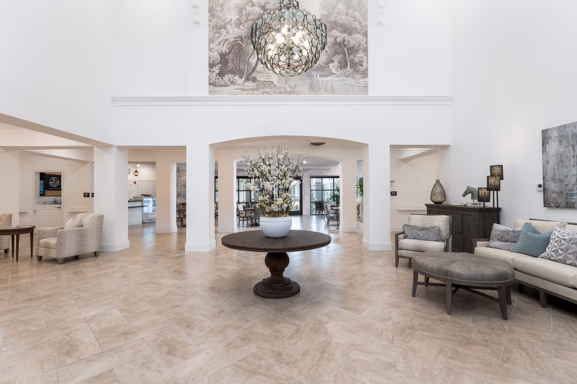 Bright, airy lobby with a central round table topped with flowers, seating areas, and a hanging decorative chandelier.