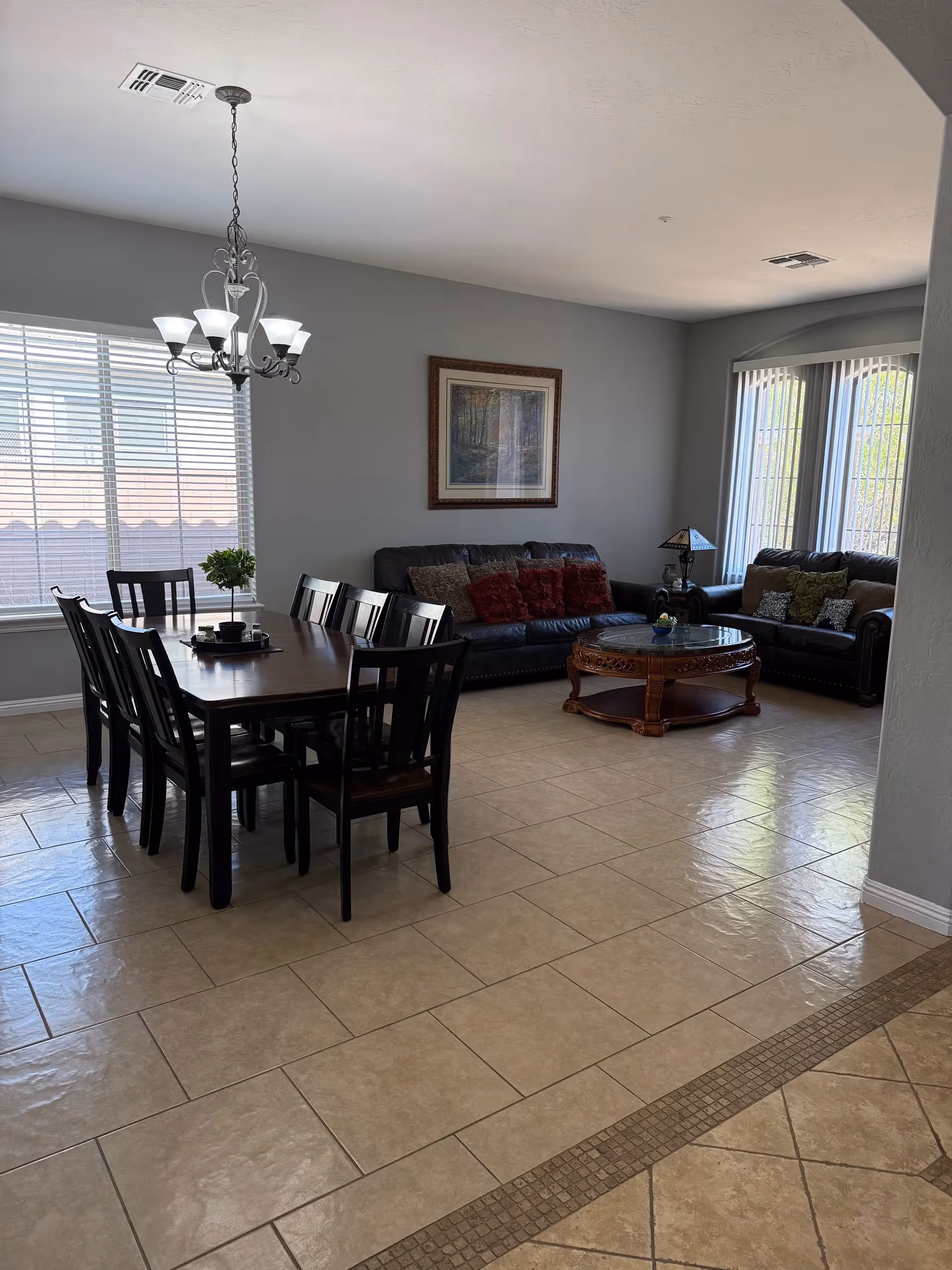 Bright dining and living area with dark wood table, chairs, sofas, and chandelier.