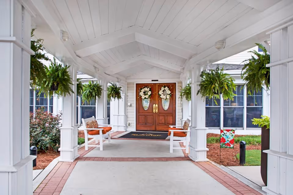 Covered entrance walkway with hanging ferns, benches, and double wooden front doors decorated with wreaths.