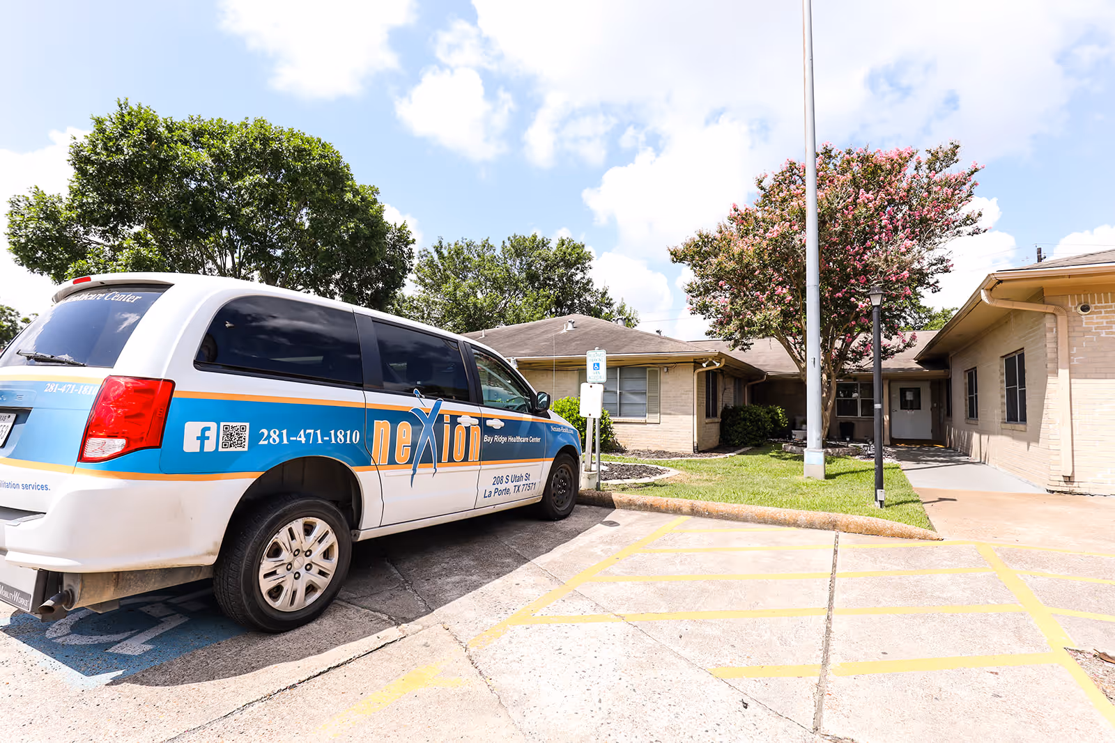 Exterior view of Bay Ridge Healthcare Center showing a single-story brick building with a tree in front and a white van parked in a handicapped parking space. The van has branding for 'Nexion' and contact information on its side.