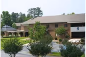 Brick two-story community building with a covered entrance, arched walkway, and landscaped trees and shrubs in front.
