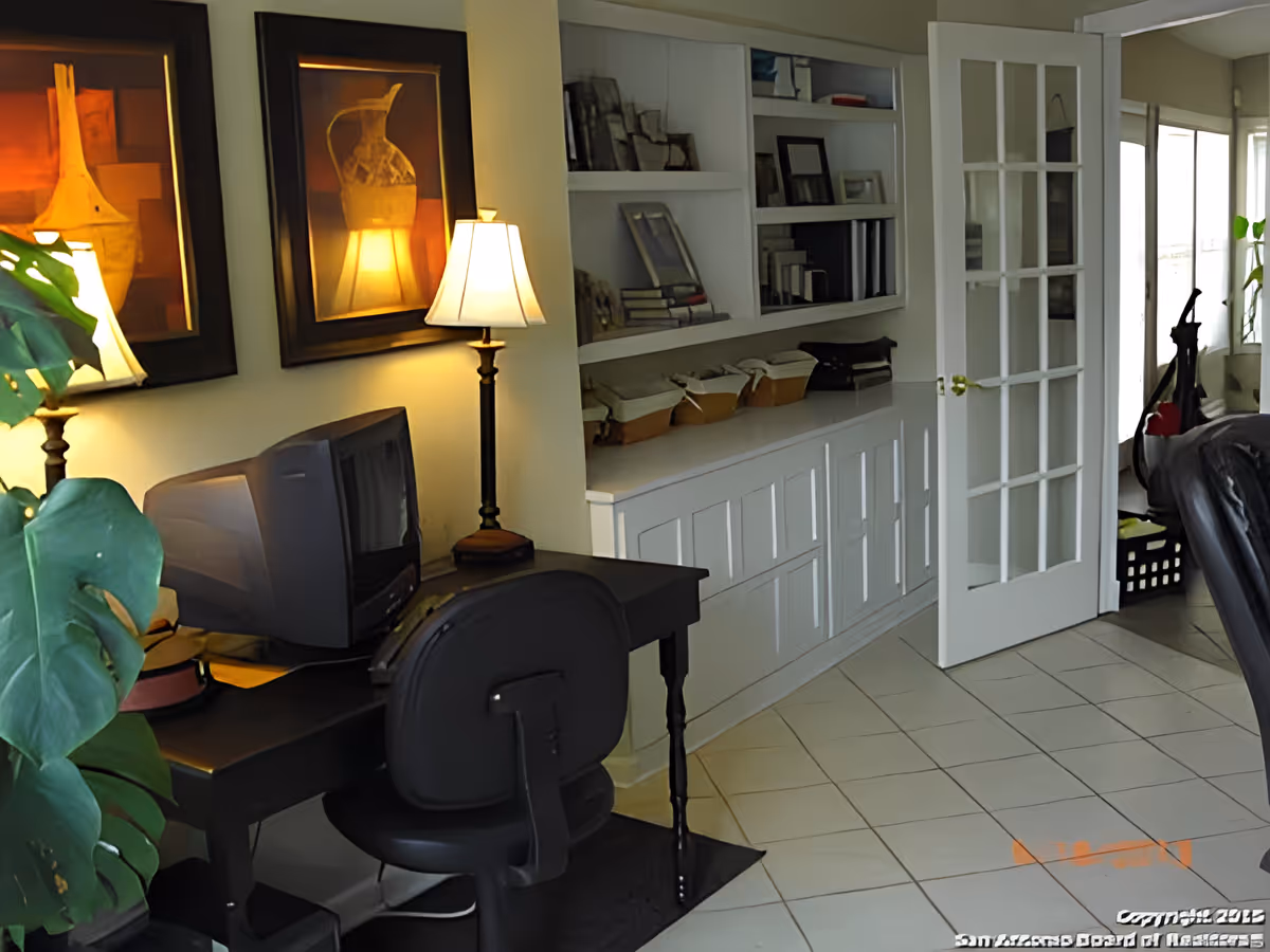 Interior living area with a desk and chair, table lamps, built-in shelves and a glass-paneled French door.