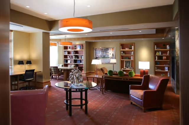 Communal lounge with armchairs, tables, bookshelves, and warm pendant lighting.