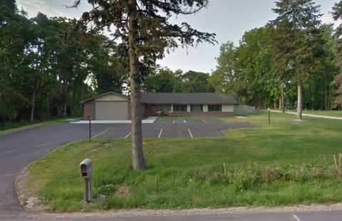 Single-story Willoughby Home exterior with parking lot, lawn, and tall trees around the building.