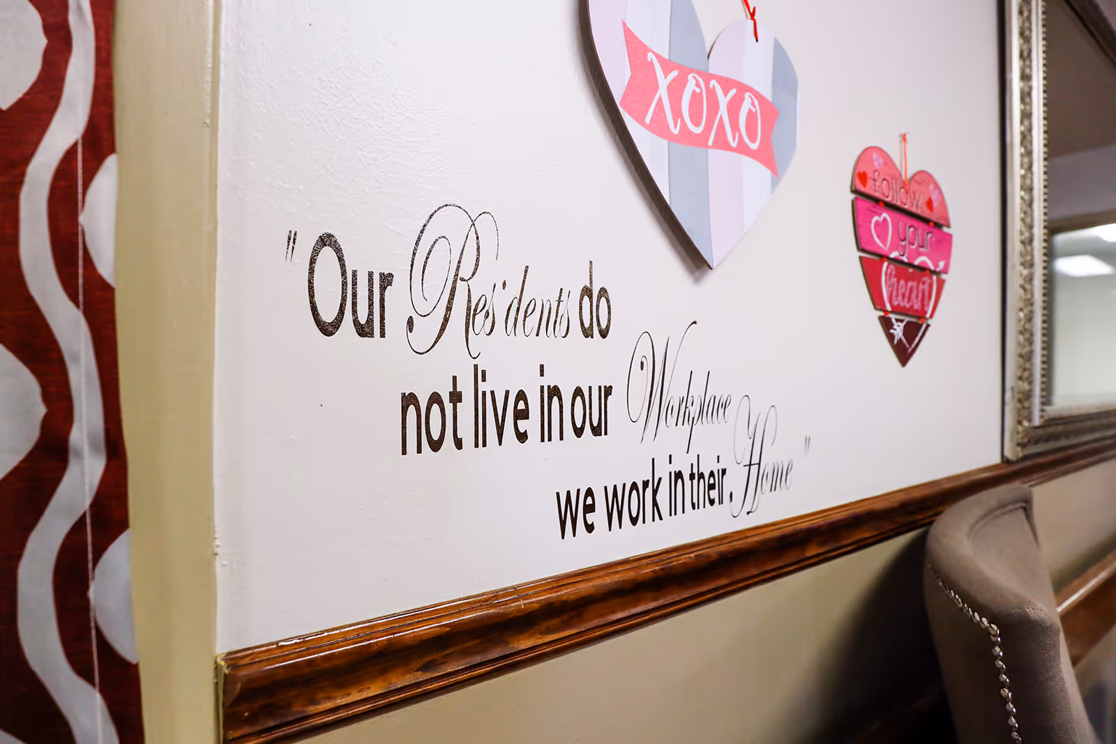 Interior wall decorated with heart signs and a large quote about residents, beside a chair and mirror.