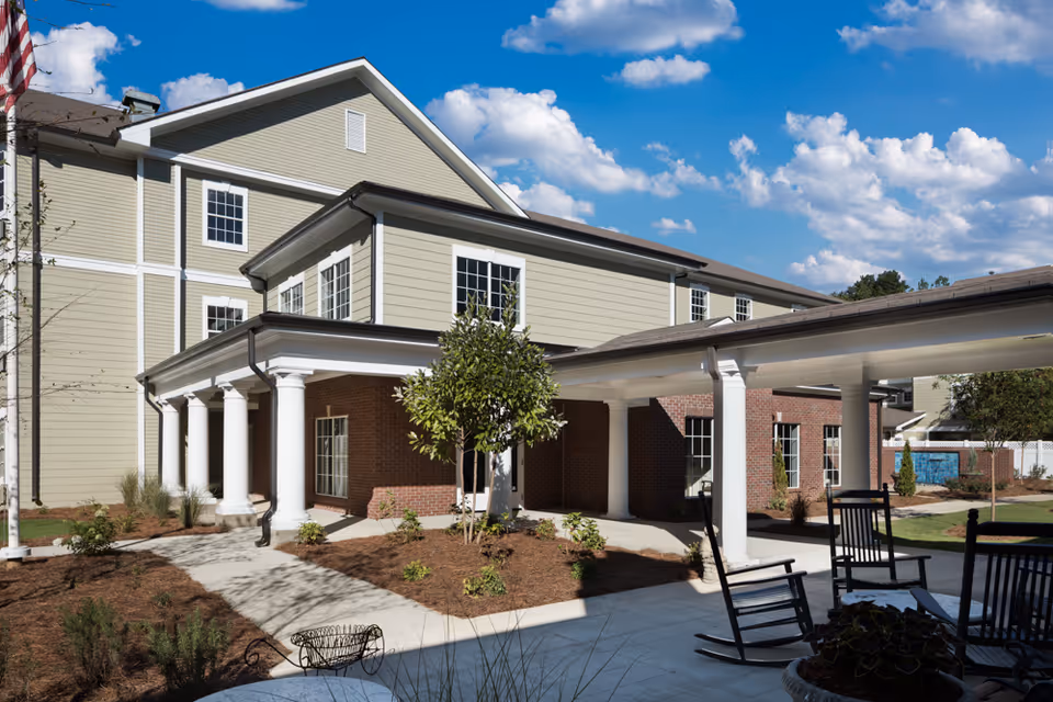 Exterior view of a Truewood by Merrill Riverchase facility with a covered entrance and seating.