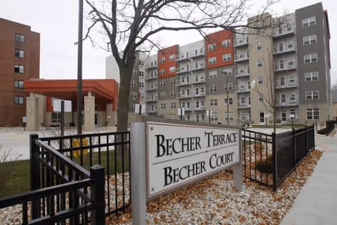 Exterior view of Becher Terrace Apartments with a sign, fence, and a multi-story building.