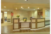 Reception lobby with a three-section wood-paneled front desk, floral arrangements, seating, and warm overhead lighting.