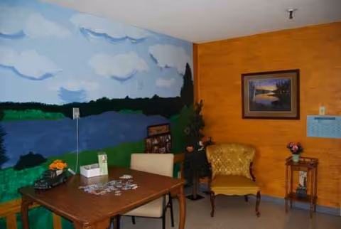A cozy living room with mural walls, orange paneling, a wooden table, and a yellow armchair.