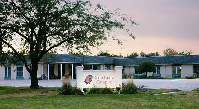 Low, single-story campus building with a front lawn, tree, and a sign reading 'Rose Lane Campus'.