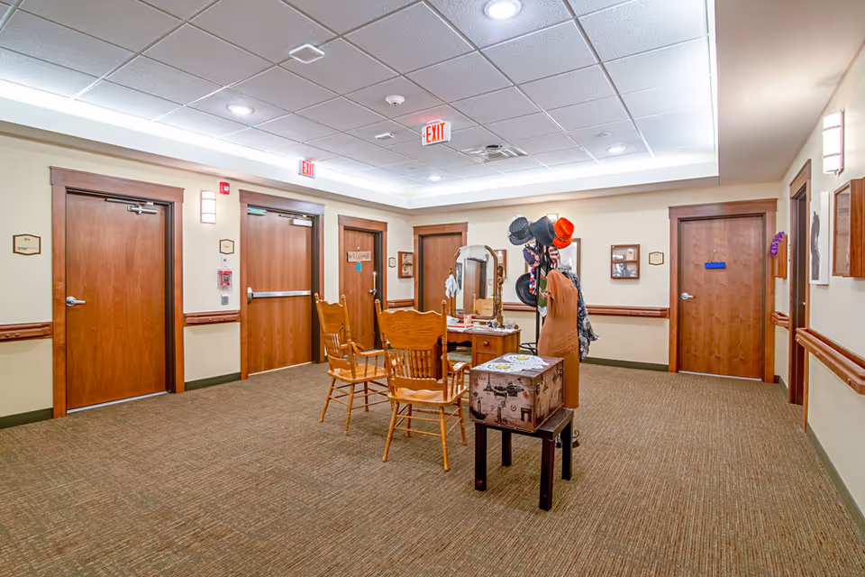 A well-lit interior common hallway with wooden doors, chairs, a vanity table and a hat rack.